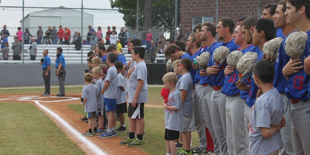 Baseball players and children stand respectfully with hands over hearts during the national anthem.