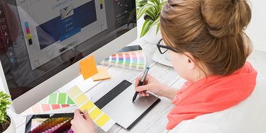 A graphic designer in front of her computer working on designing a printed item.