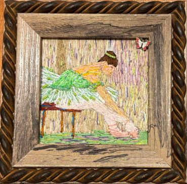 Embroidery art of a ballerina adjusting her shoe in a wooden frame.
