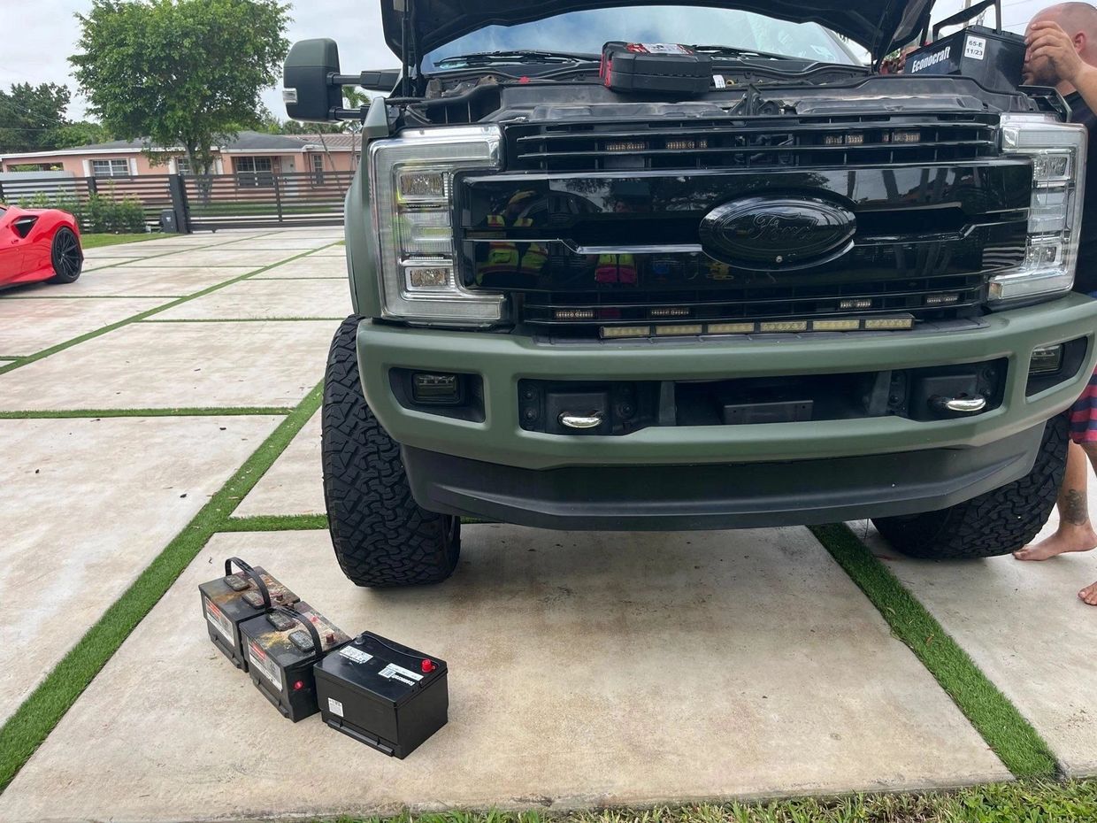 A truck with its hood open and batteries on the ground.