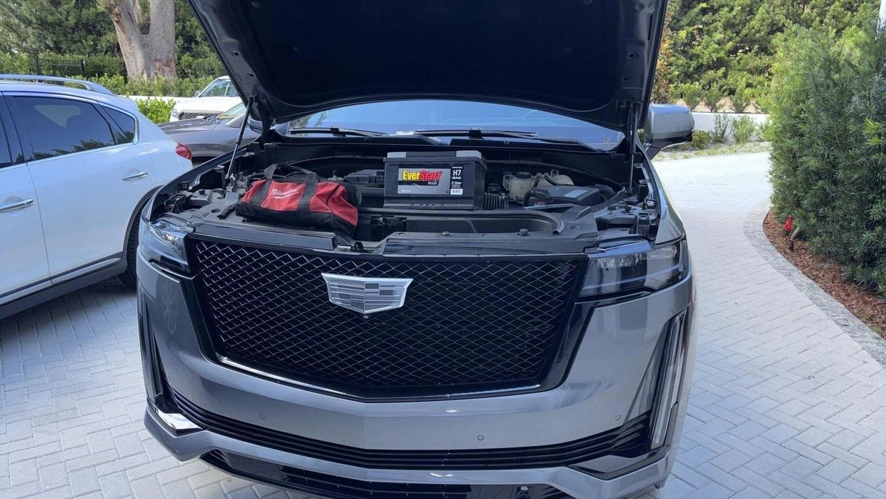 Cadillac SUV with hood open showing engine and battery.