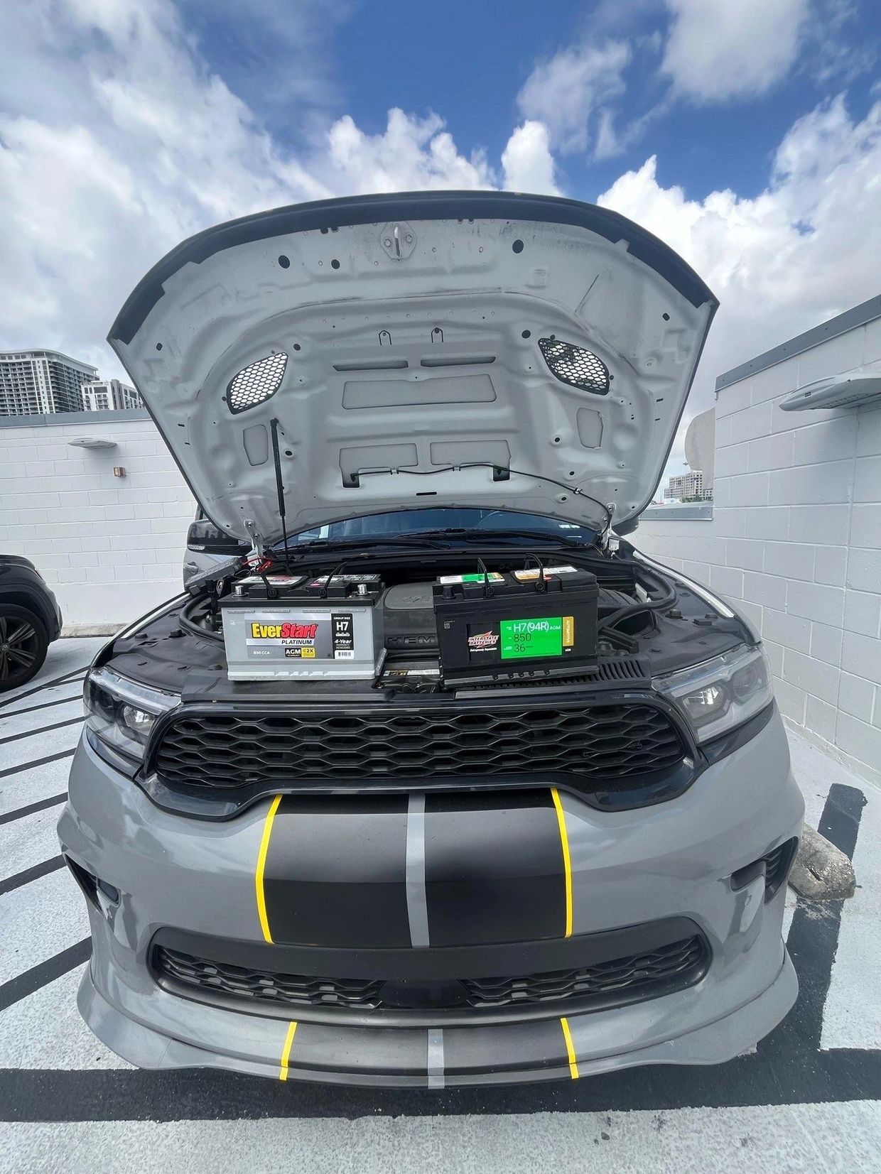 Open car hood showing two car batteries side by side on the engine.
