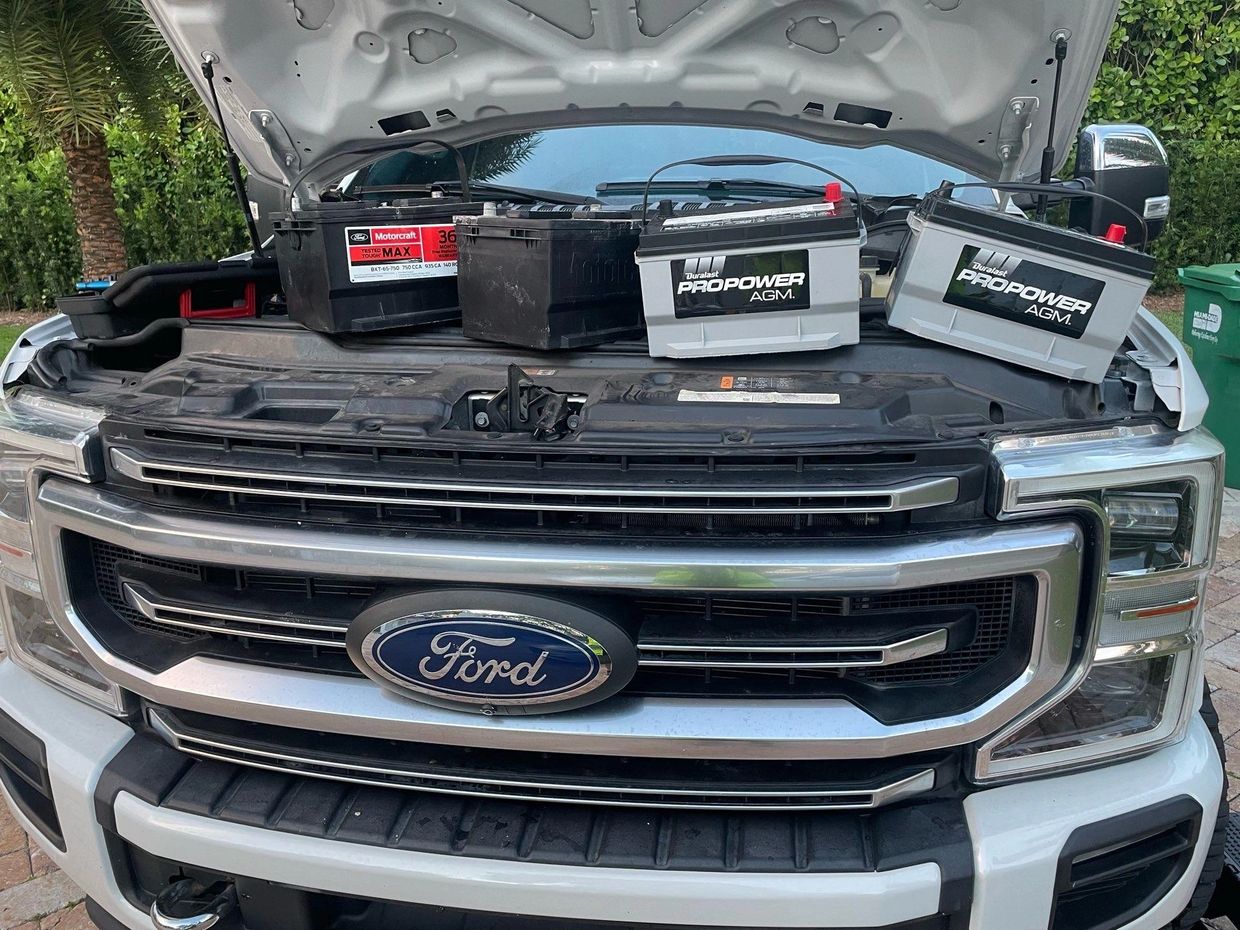Four car batteries placed on a Ford truck with the hood open.