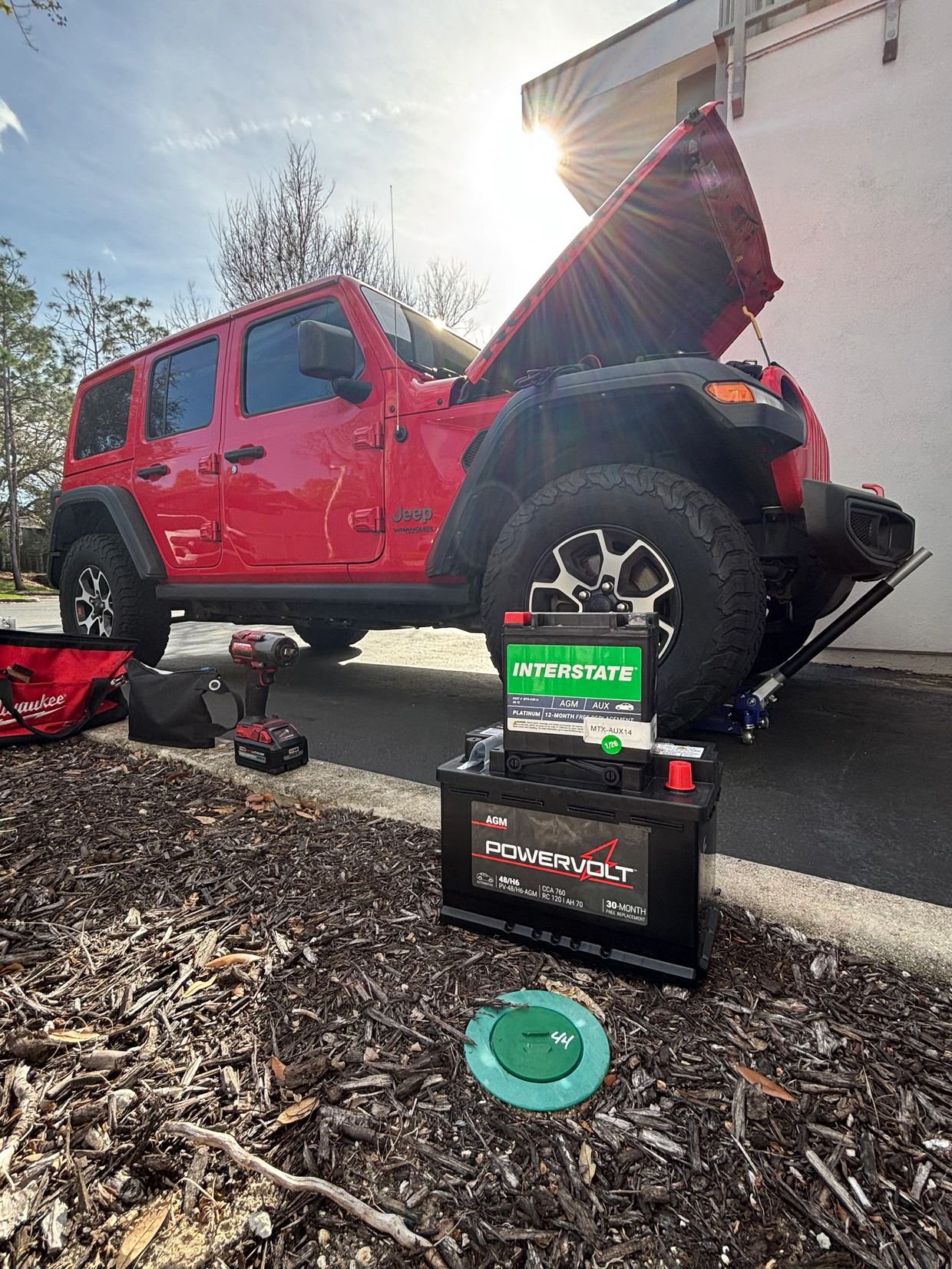 Red Jeep Wrangler with hood open, battery replacement in progress.