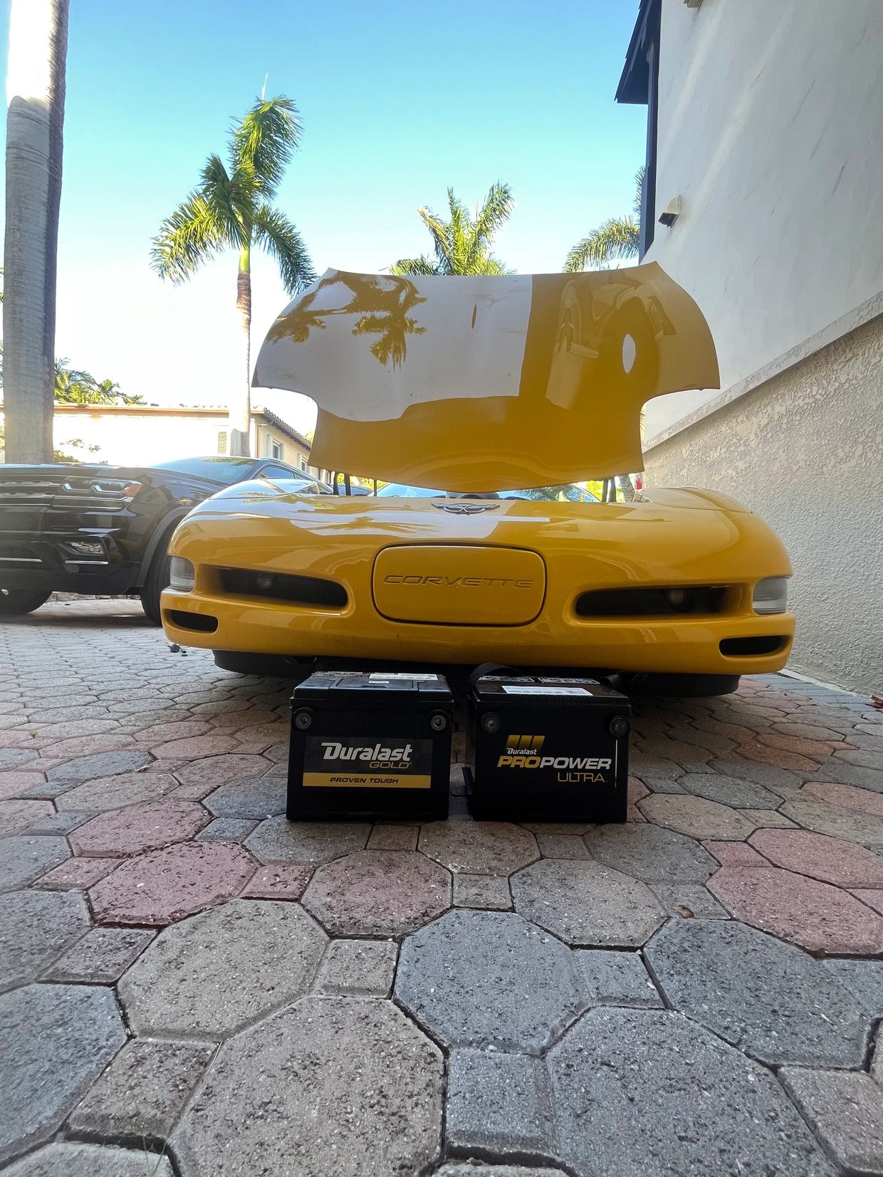 Yellow Corvette with its hood open, two car batteries in front.