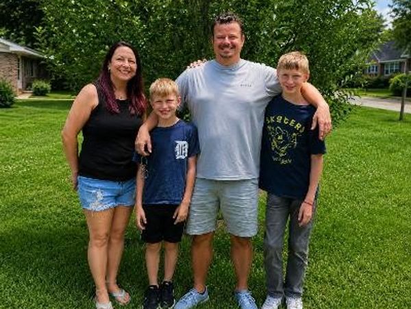 Family of four posing outdoors on green grass.