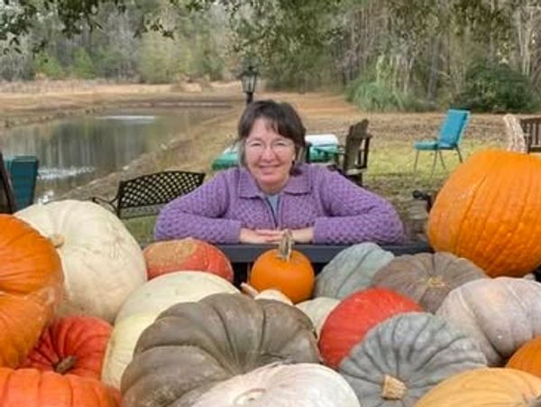 Woman smiling behind a large assortment of pumpkins outdoors.