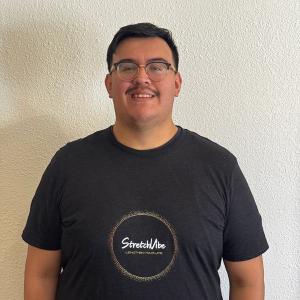 Man smiling wearing glasses and a black StretchVibe t-shirt against a white wall.