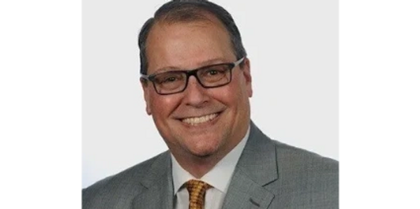 Smiling man in gray suit and glasses with a yellow tie.