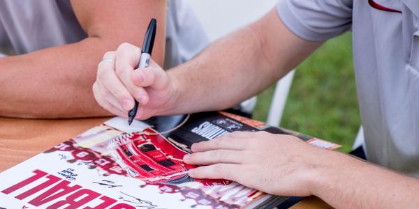 A person signs a sports magazine with a black marker.