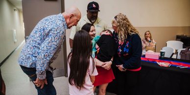 A family warmly greeting a young child at an indoor event.