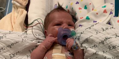 Newborn baby in hospital with pacifier and monitoring wires.
