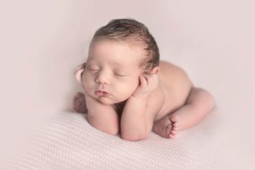 Sweet newborn baby girl with her head on her arms, sleeping and naked, on a soft pink background