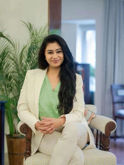 A woman sitting cross-legged on a chair, smiling into the camera.