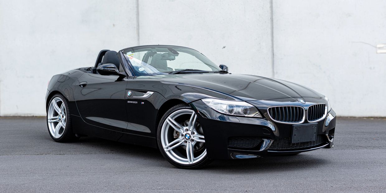 Black BMW Z4 convertible sports car parked on pavement with white wall background.