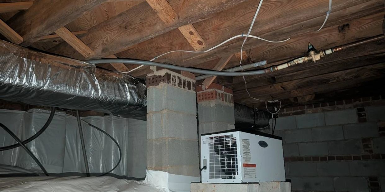 Crawlspace liner with a raised dehumidifier beneath exposed floor joists.