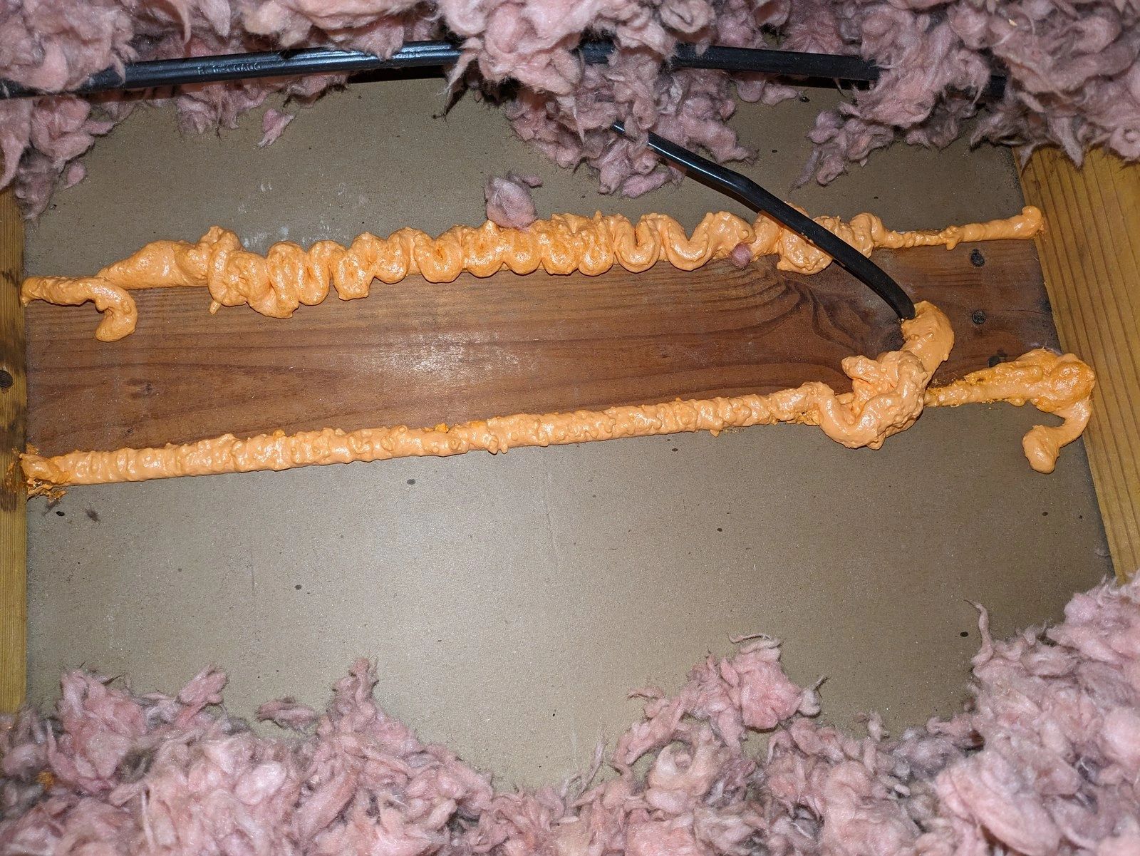 Orange foam seals wood framing seams and a wire opening, with pink insulation around the edges.