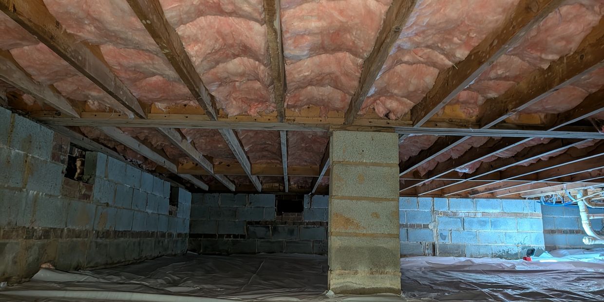 Crawlspace floor liner beneath fitted insulation, with exposed masonry walls and pier.