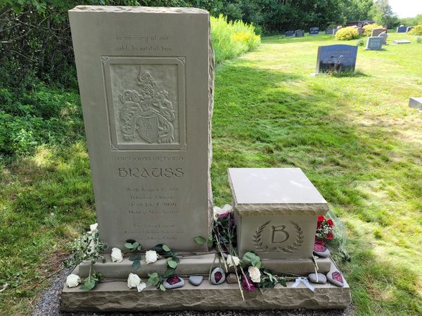 A gravestone memorial with flowers and engraved crest in a green cemetery.