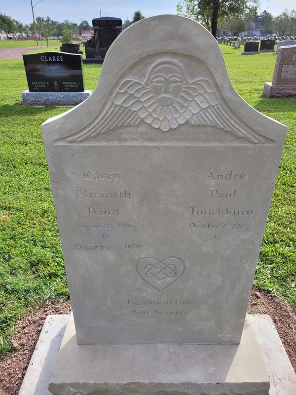 Stone gravestone with winged face carving and names Karen Elizabeth Baird and André Paul Touchburn.