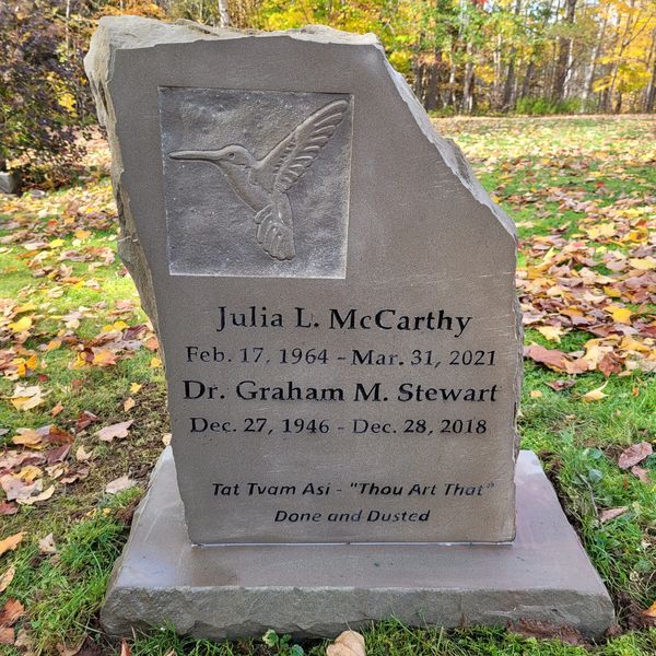 A gravestone with a hummingbird engraving and inscriptions for Julia L. McCarthy and Dr. Graham M. Stewart.