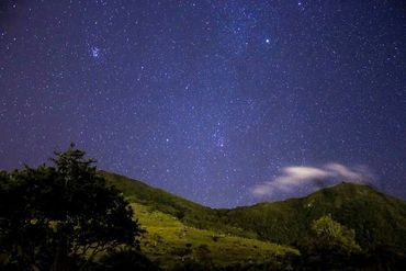 Starry night sky above green hills and trees.