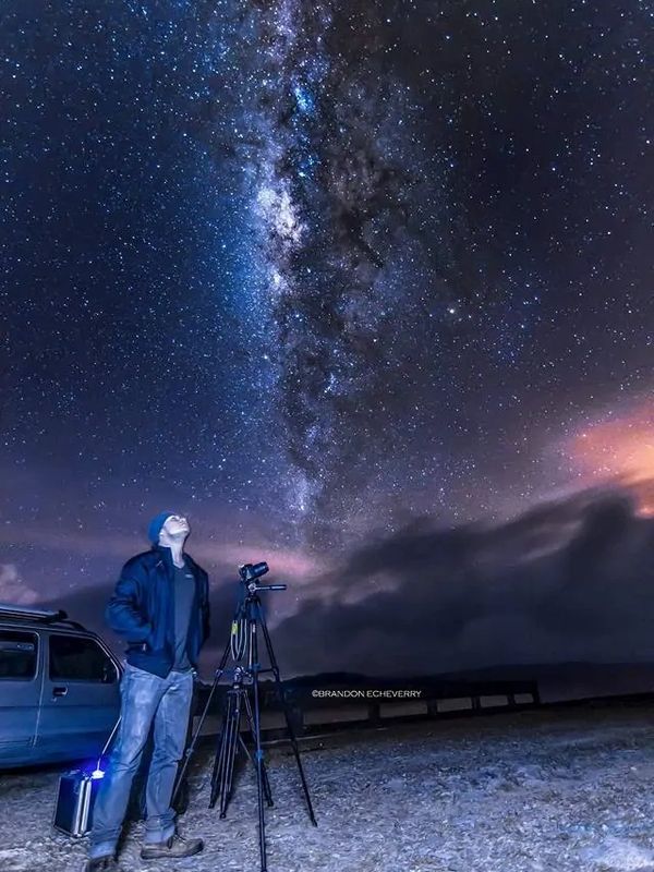 A man stargazing through a telescope under a vibrant Milky Way sky.