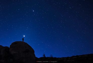 Person holding light on a rocky hill under a starry night sky.