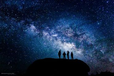 Four people silhouetted against a star-filled night sky with the Milky Way.