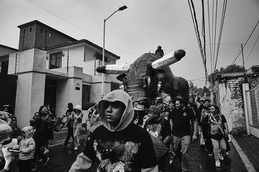 Black and white photo of a street parade with a large bull figure and crowd.