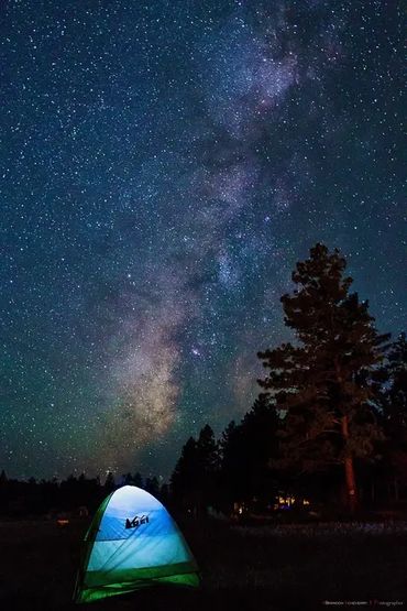 A glowing tent under a star-filled night sky with the Milky Way visible.