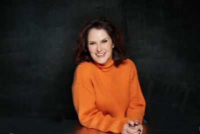 Audrey Federici smiling in an orange sweater against a dark background.