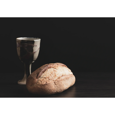Loaf of bread and a goblet on a dark surface.