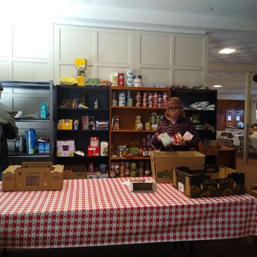 Person organizing canned goods on shelves behind a table with boxes.