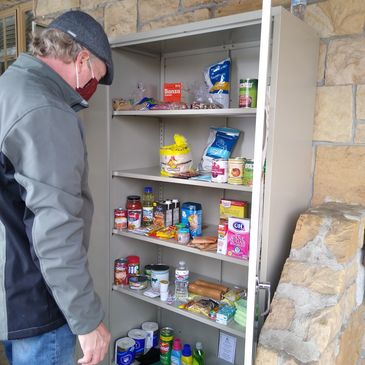 A man wearing a mask looks at a stocked food pantry cabinet.