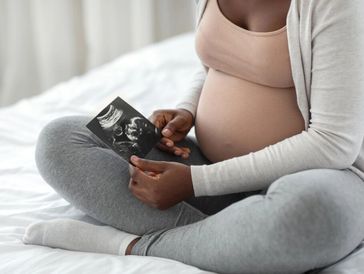 Pregnant woman sitting on bed holding an ultrasound image.