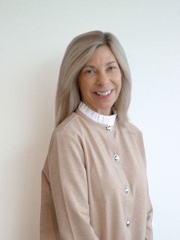 Smiling woman with light blonde hair wearing a beige cardigan and white blouse.