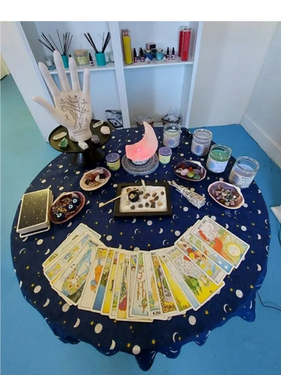 A table in Ashley's office with tarot cards laid out, a palm reading diagram, candles, sage, & gems.