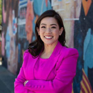 Woman smiling confidently in a bright pink blazer.