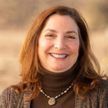Smiling woman with brown hair in outdoor setting.