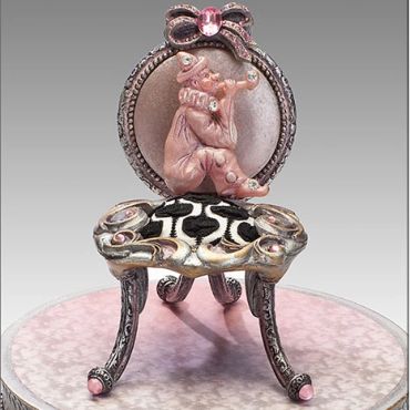 Miniature chair with a pink clown figure and ornate design.