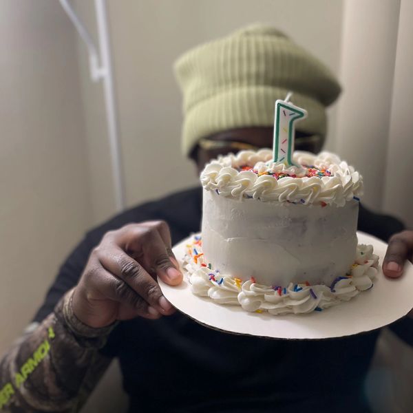 Person holding a white cake with a "1" candle.