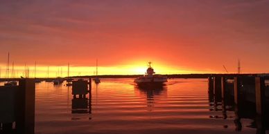 A serene sunset over a calm harbor with boats and docks.