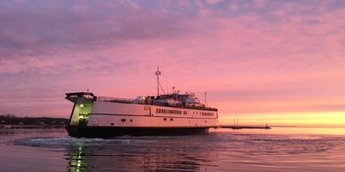 Ferry boat sailing during a colorful sunset over calm waters.