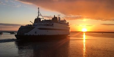 Ferry sailing at sunset with vibrant sky colors reflecting on the water.