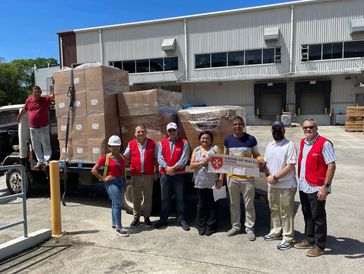 Group of people posing with a truck full of boxed supplies outside a warehouse.