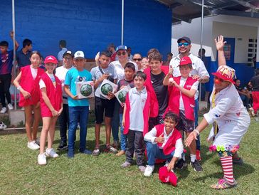Group of kids and adults posing outdoors with sports balls and a clown.
