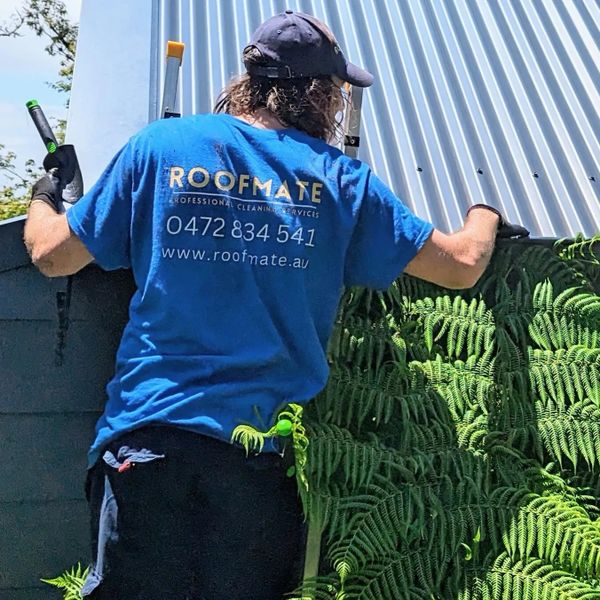 Person wearing a Roofmate shirt working on a corrugated metal roof.