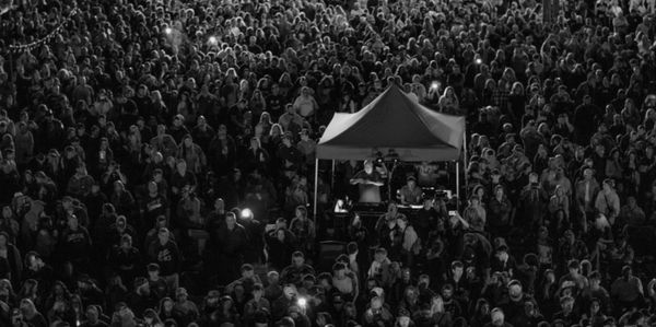 A large crowd gathered behind a tent at a night event.