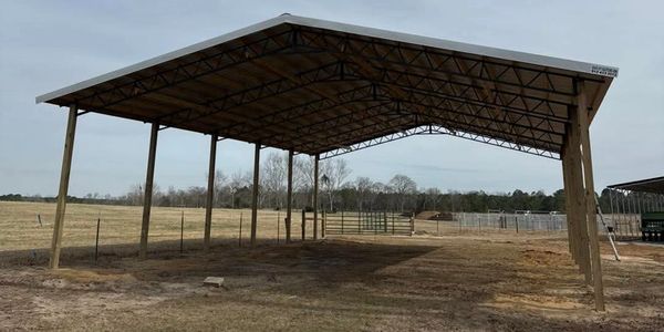 Large open-sided metal roof structure on wooden posts in a field.